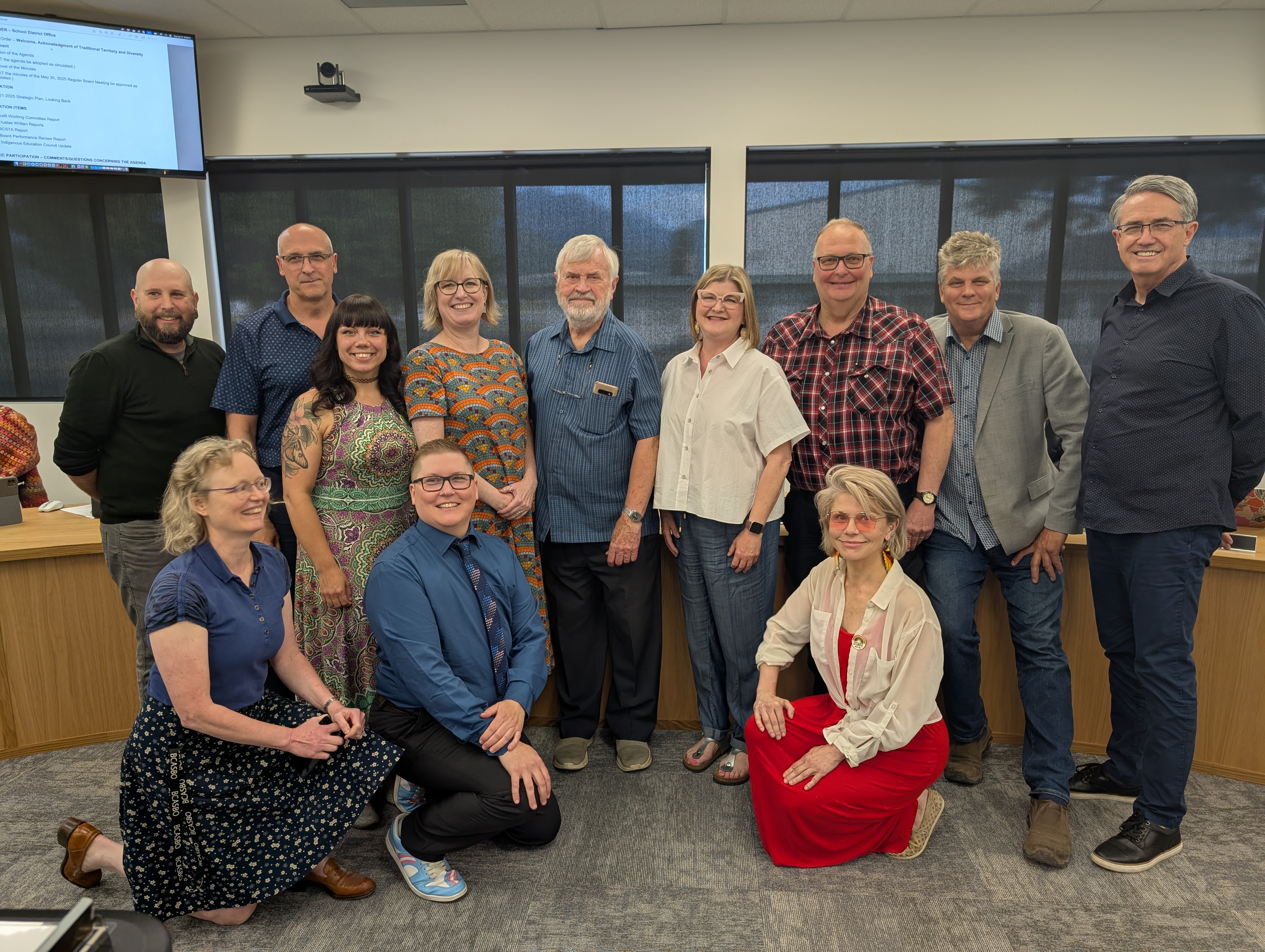 A group of people gather in front of a board table. They are smiling. 