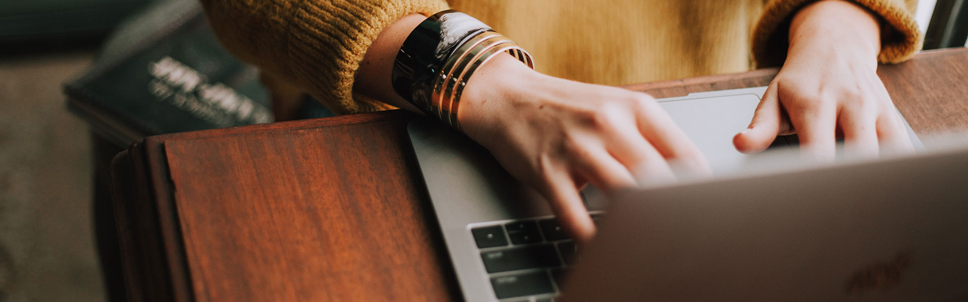 Two hands type on a silver laptop. 