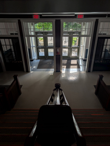A staircase leads to a set of double doors with light coming through the windows. 