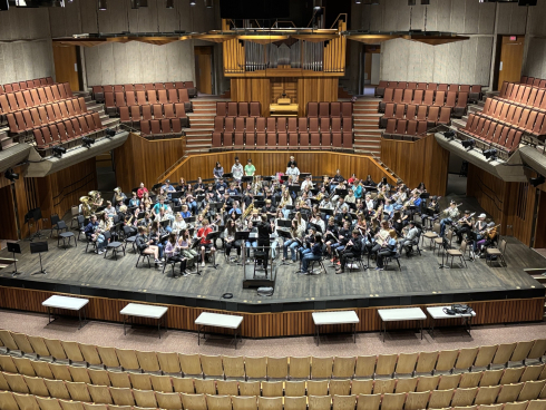 A group of young people play instruments in the middle of a room surrounded by chairs.