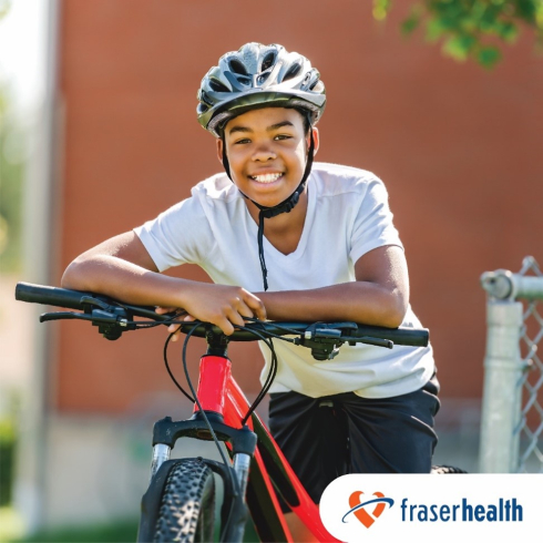 A Black youth in a white shirt rests on a bright red bike. He is wearing a helmet. 