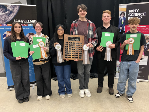 A group of students display their ribbons and awards in front of science banners.