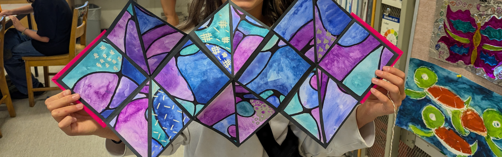 A long colourful piece of artwork is displayed by two hands. 