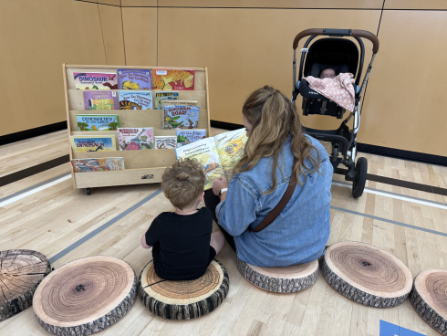 An adult and a child sit on cushions and read a book together. 