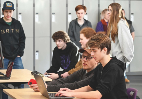 A group of students and an adult work on computers. 