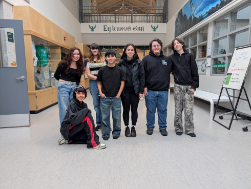 A group of students gather in the hallway of their school. They are smiling. 