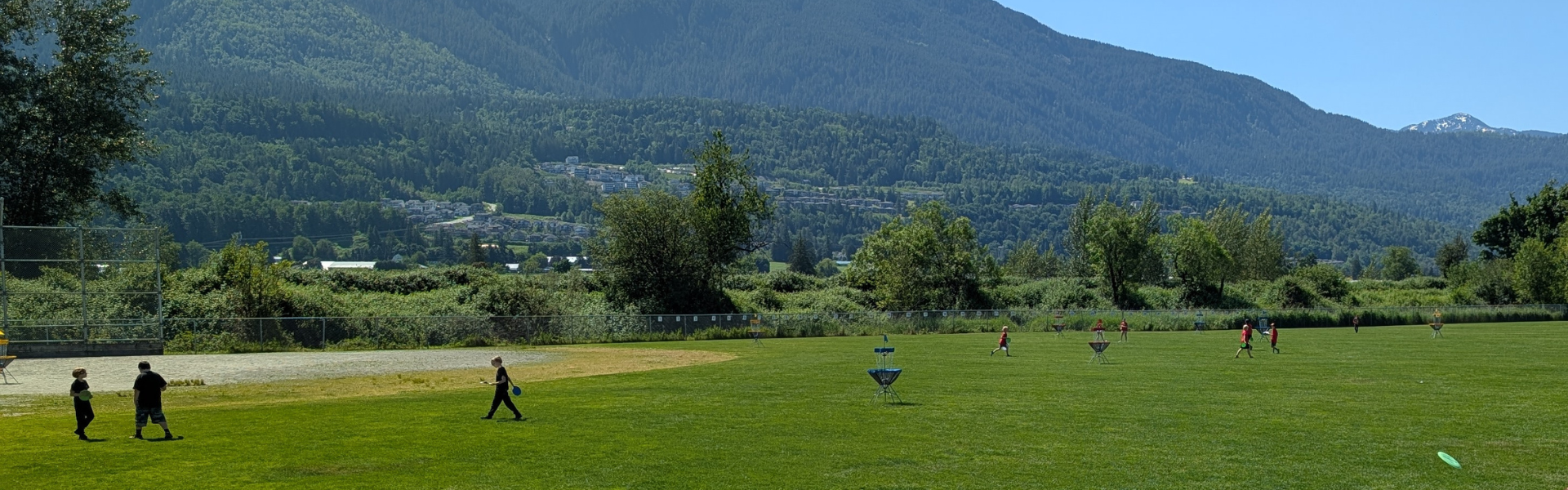 Students run on a field. The sky is blue and there are sloping mountains in the background. 