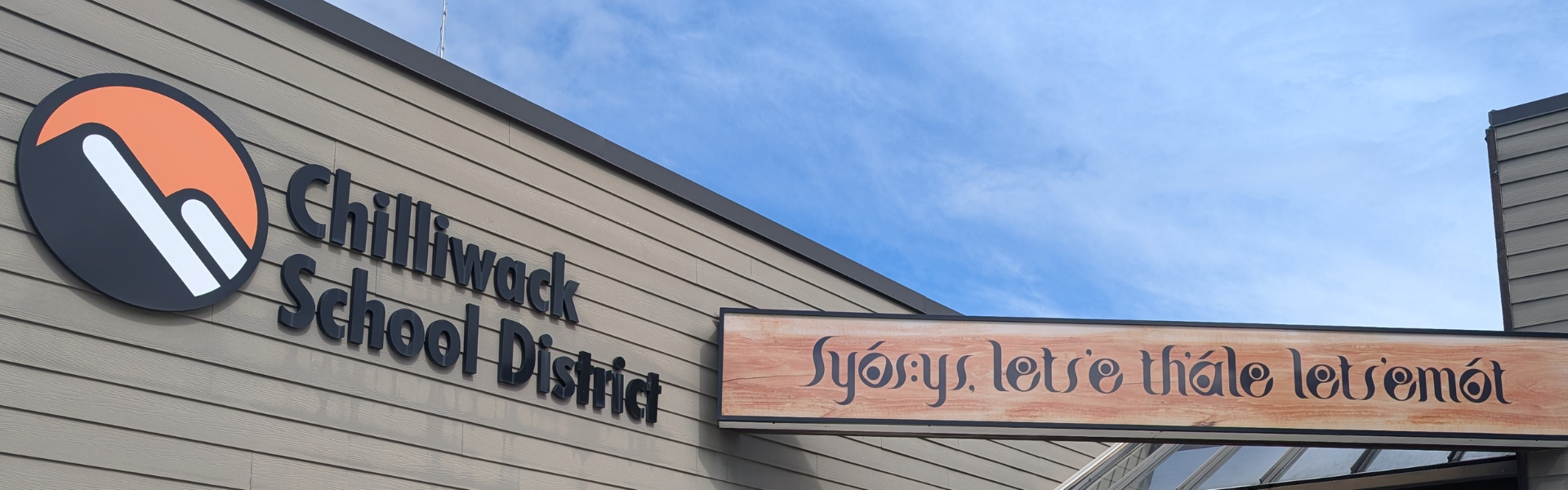 The top of a brown building which features the Chilliwack School District logo.