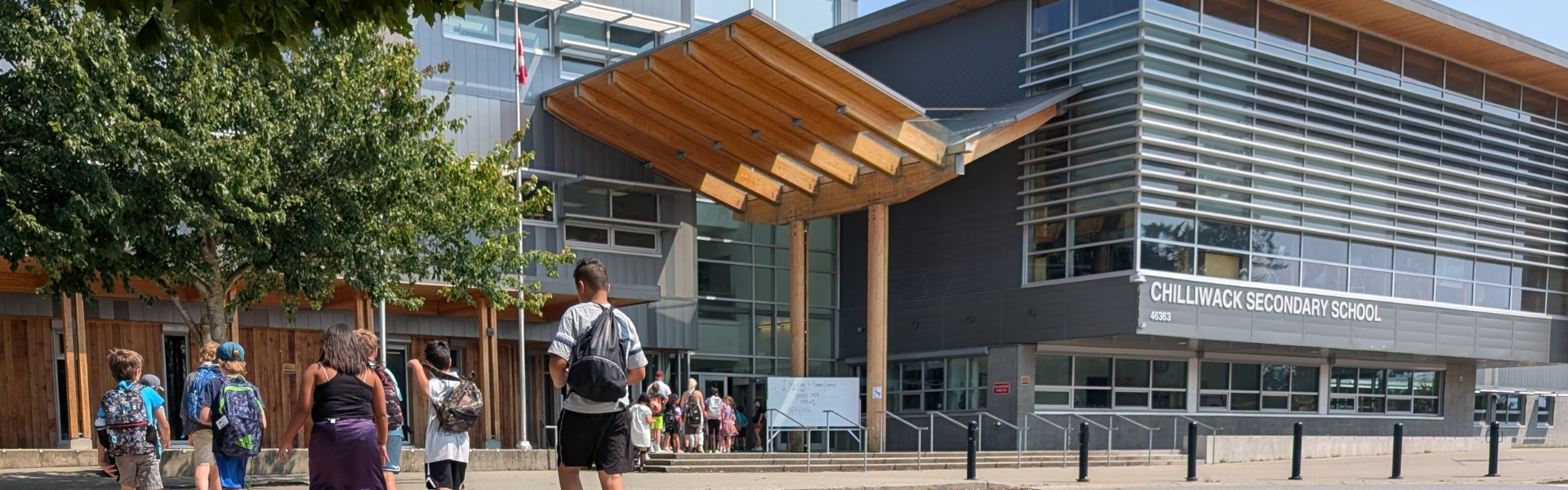 A group of students walk towards a grey school building on a sunny day. 
