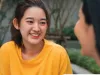 A girl wearing a yellow shirt is smiling as she talks to a peer. 