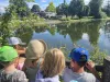 Children gather together and are looking out over a pond. It's sunny. Most are wearing hats. 